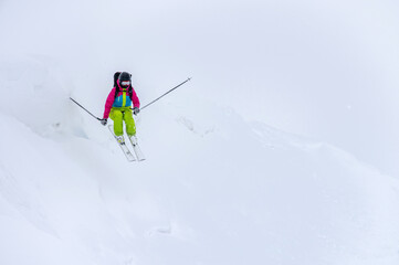 A young female skier rides a snowy mountainside drop in poor visibility. Bad weather skiing concept