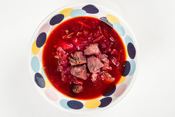 Borscht with meat in a colored plate on a white background
