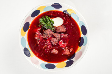 Borscht with meat in a colored plate on a white background