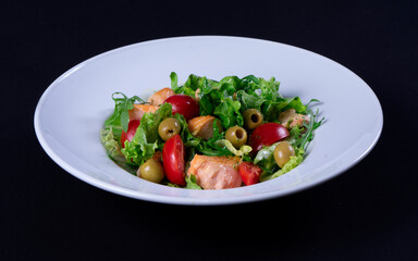 Fresh salmon salad, cherry tomatoes, olives, green lettuce, arugula in a white plate on a black background