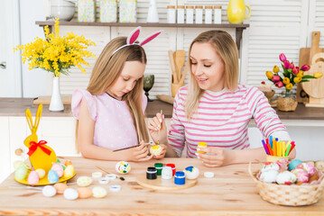 Happy easter. A mother and her daughter painting Easter eggs. Happy family preparing for Easter. Cute little child girl wearing bunny ears on Easter day.