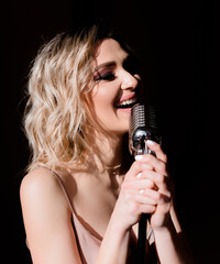 Close up of blonde woman holding a microphone and singing on the black background isolated.