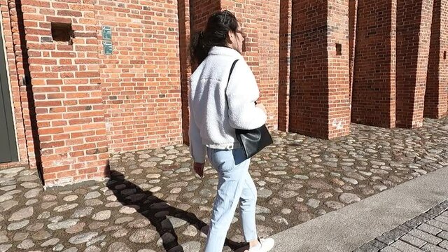 the girl walks along a brick wall on a sunny day