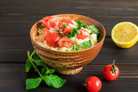 Fresh home-made tabouli, or tabbouleh salad, with its ingredients, side view on dark wooden background