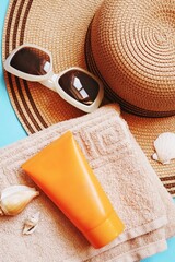 Summer travel flat lay photography. Sun hat, sunglasses, towel, sunscreen tube and seashells. Cosmetic products for skin care