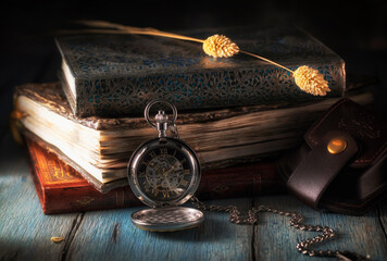 Pocket watch near a stack of books on a blue wooden table