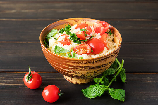 Fresh home-made tabouli, or tabbouleh salad, with its ingredients, side view on dark wooden background