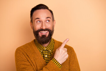 Photo of positive cheerful mature man point index finger empty space for adverts promotion isolated over beige color background