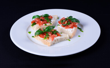 Sandwich with cream cheese, tomatoes, mint, basil in a white plate on a black background