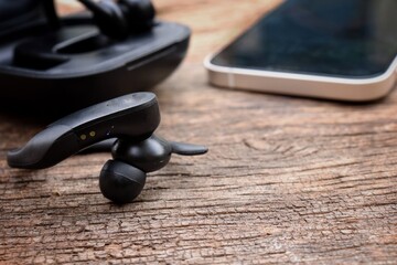 Black wireless bluetooth earphones and smart phone on wood background
