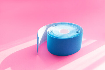 Close up blue roll of kinesiology tape on pink background with trendy sun light and shadows. Recovery, anti-aging procedures concept. Kinesio taping
