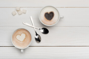 top view of cups with cappuccino and latte near spoons and sugar cubes on white wooden background