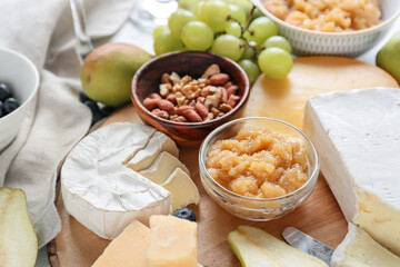 Tasty pear jam with different cheeses and nuts on table