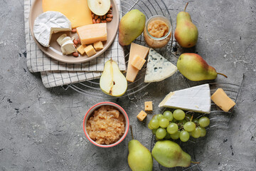Tasty pear jam with different cheeses on grunge background