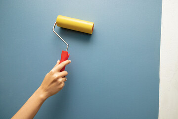 Hand of a woman smoothes air and glue bubbles on the wallpaper with a roller. Renovation Equipment...
