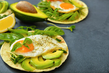 Tasty fried egg with avocado and flatbread on dark background