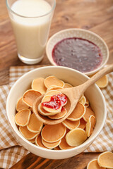 Bowl with tasty mini pancakes with jam and milk on table