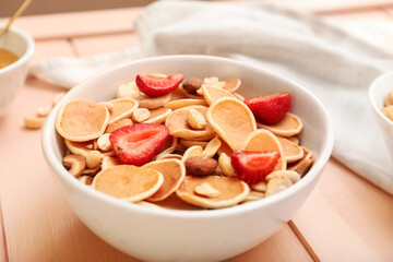 Bowl with tasty mini pancakes and strawberry on table