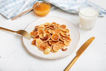 Plate with tasty mini pancakes, honey and milk on white background