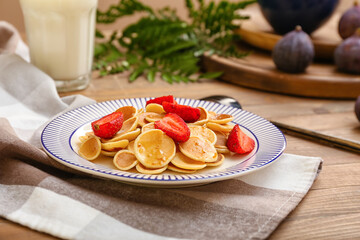 Plate with tasty mini pancakes and strawberry on table
