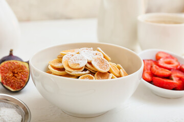 Bowl with tasty mini pancakes on table
