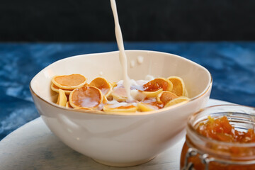 Pouring of milk into bowl with tasty mini pancakes on table