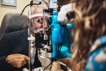 Elegant senior bearded man receiving ophthalmology treatment. Doctor ophthalmologist checking his eyesight with modern equipment.