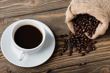 top view of sack bag with roasted coffee beans near cup on wooden surface