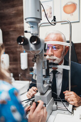 Elegant senior bearded man receiving ophthalmology treatment. Doctor ophthalmologist checking his eyesight with modern equipment.