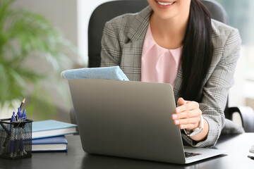 Young businesswoman cleaning laptop in office