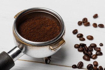 Close up of metallic portafilter with ground coffee near beans on white