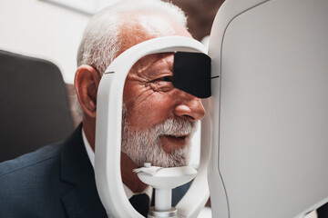 Elegant senior bearded man receiving ophthalmology treatment. Doctor ophthalmologist checking his...