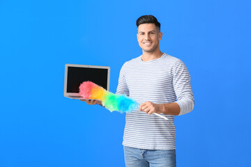 Young man with laptop and dust brush on color background