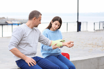 Young woman applying bandage on mature man's arm outdoors