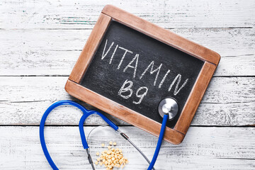 Stethoscope, folic acid pills and text VITAMIN B9 on wooden background