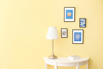 Lamp on table near color wall with stylish pictures