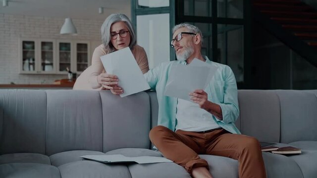 Modern senior couple in casual clothing taking care of their finances while bonding together at home