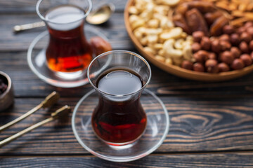 Two glasses of black strong turkish tea, platter board with nuts : cashews, almonds, dates, hazelnuts. Low sugars diet snack. Wooden plate, dark background. Slow life, Healthy tea break relax concept