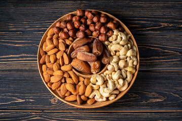 Natural organic raw nuts wooden plate on dark background top view. Platter board with healthy snack: cashews, almonds, dates, hazelnuts. Low sugars diet food. Norm of fats and oils, keto diet