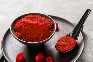 Bowl and spoon with red chili powder on grey background