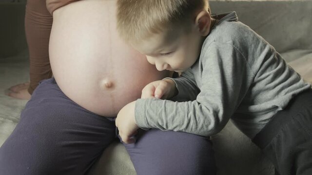 pregnant woman sitting on couch, little boy listens to baby movement in belly