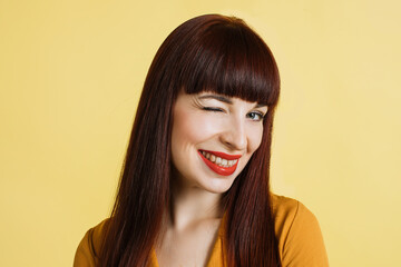 People, emotions, facial expressions. Close up portrait of jolly, vivacious sttractive young woman long straight red hair, winking to camera with smile, on isolated yellow background