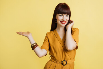 Portrait of beautiful girl in yellow dress, showing imaginary something, empty copy space for some...