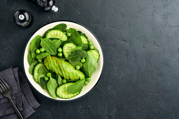 Green vegetable salad with spinach, avocado, green peas and olive oil in bowl on dark slate, stone or concrete background. Top view with copy space. Green vegetables for diet concept.