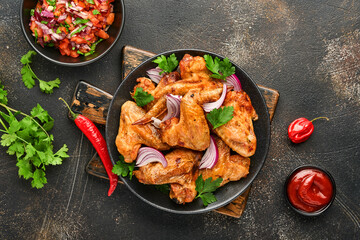 Grilled chicken wings or roasted bbq with spices and tomato salsa sauce on a black plate. Top view with copy space.