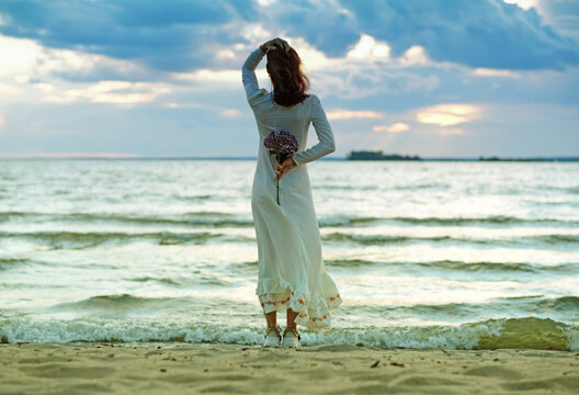 A girl in a white wedding dress stands with her back to the Stormy Sea. A conceptual picture about loneliness, hopes and expectations