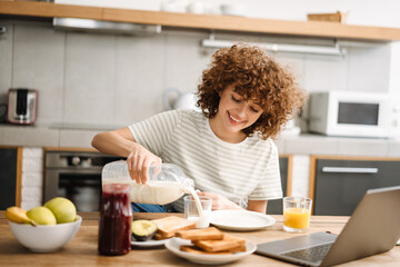 Smiling young woman having breakfast while sitting at table in kitchen