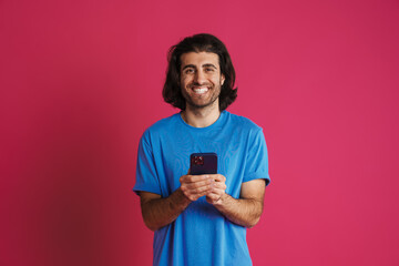 Unshaven brunette man in t-shirt using mobile phone and smiling