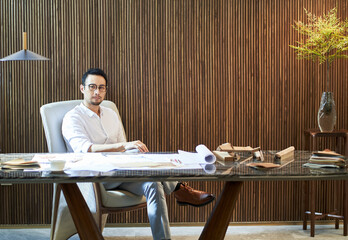 Asian bearded designer sitting, thinking and sketching ideas indoors