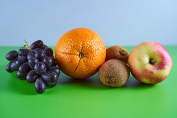 Ripe blue grapes, orange, kiwi and apple on a gray green background